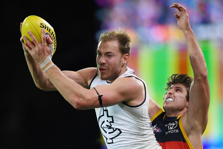Carlton forward grabs the ball in two hands in front of him as an Adelaide defender grimaces behind him.