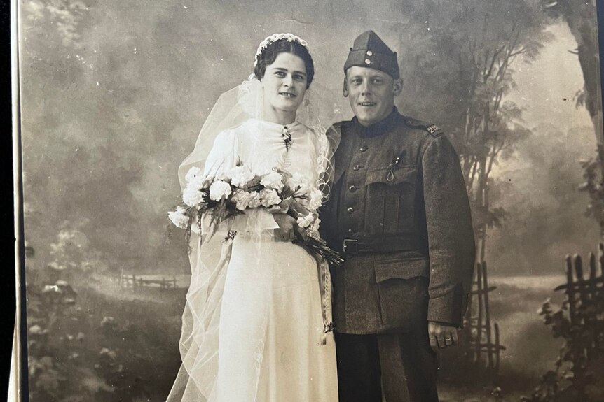 A black and white studio photograph depicts a man in uniform and woman in white on their wedding day.