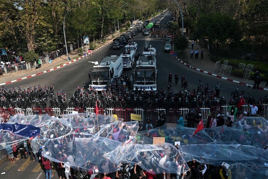 A large group of protesters use plastic to cover themselves as riot police use a water cannon in an attempt to disperse them.