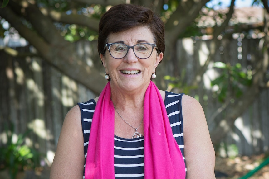 Woman with vibrant scarf stands behind chair in garden and smiles.