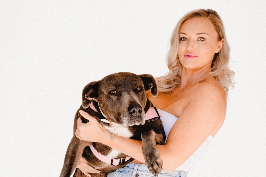 A woman in cut off denim shorts holding a dog against with a white background.