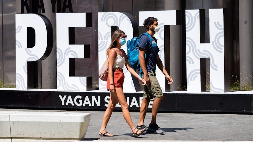 Two people wearing masks walk past a large Perth sign in Yagan Square.