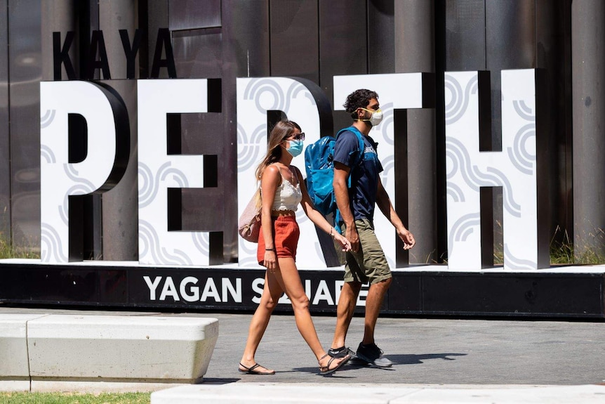 Two people wearing masks walk past a large Perth sign in Yagan Square.