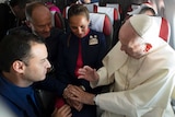 Close shot of the Pope blessing a couple seated in an aeroplane.