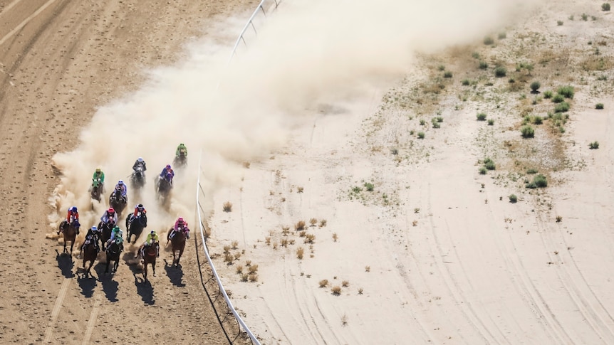 An aerial shot of horses and riders tearing around a dusty outback racetrack.