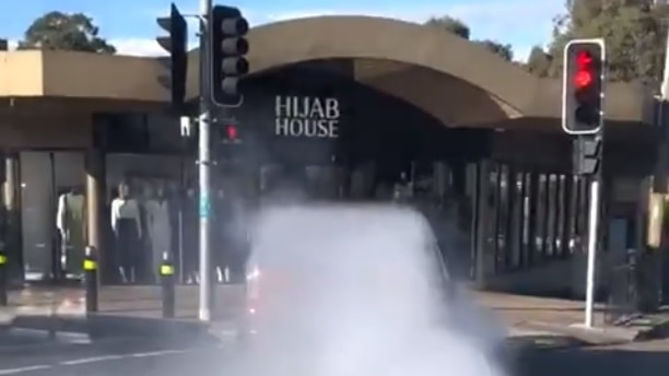 A large plume of smoke behind a car, heading towards a shop