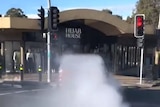 A large plume of smoke behind a car, heading towards a shop