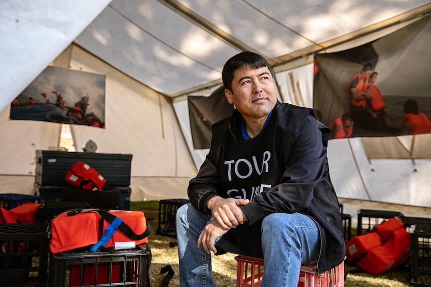 Asad sits on a milk crate inside a medical tent and looks off camera