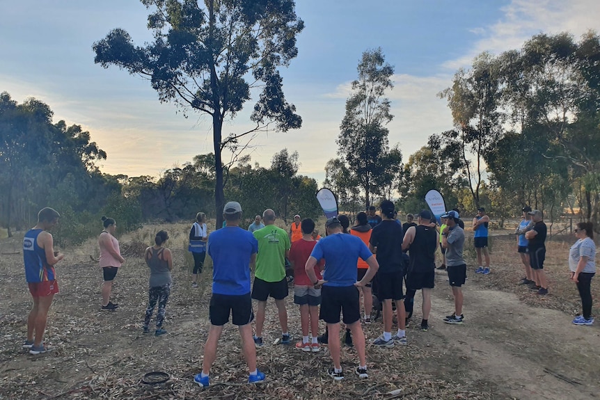 les participants au parkrun sont debout en groupe et écoutent un briefing des bénévoles avant de commencer leur course.