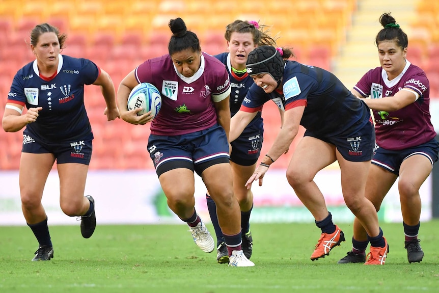 A Queensland Super W player holds the ball as she makes a break against the Rebels.