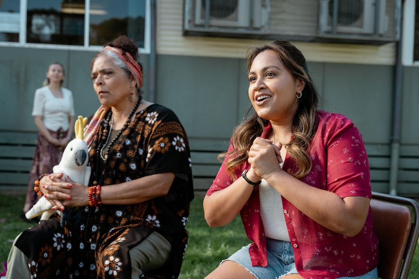 A film still of Lisa Maza and Jessica Mauboy, two Aboriginal women. They are sitting outside, Mauboy with her hands clasped.