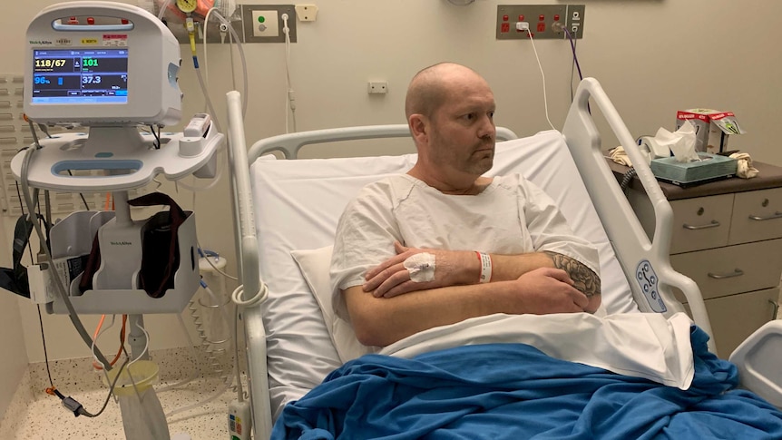 Dave Roberts sitting up in his hospital bed surrounded by equipment