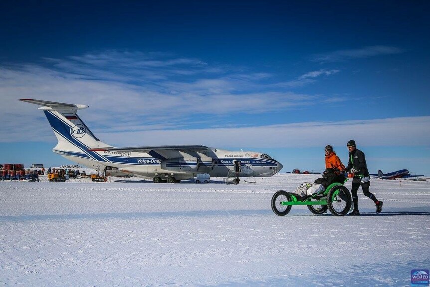 Johanna Garvin and her team run over snow in front of a parked plane.