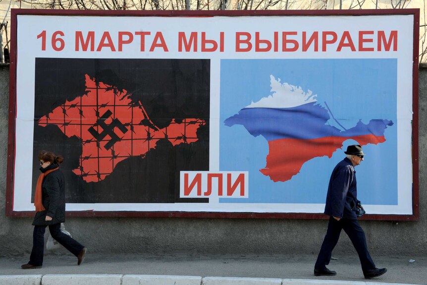 People walk past a poster in Crimea
