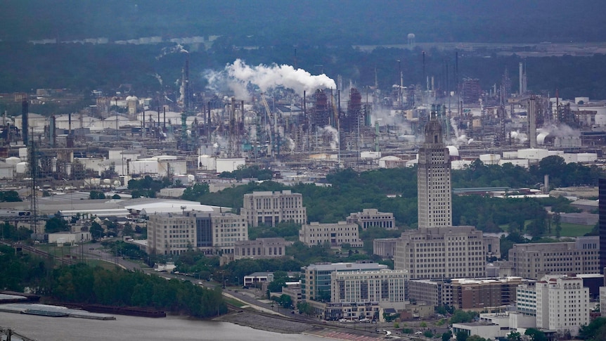 An aerial shot of an oil refinery spewing smoke beyond a city.