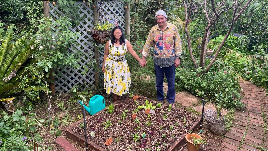 Two people holding hands in front of a garden bed.