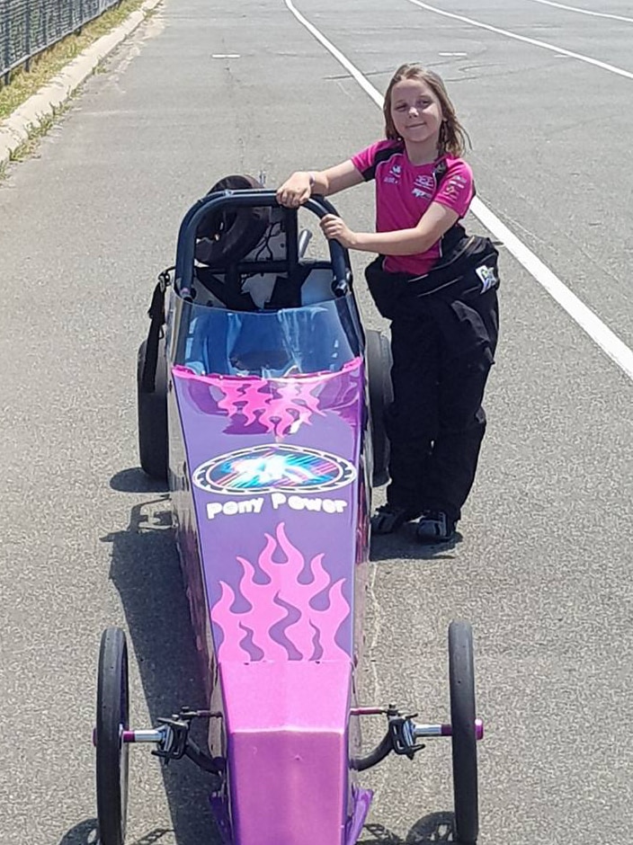 Eight-year-old Anita Board standing next to her pink and purple junior drag car on the tarmac at Perth's Kwinana Motorplex.