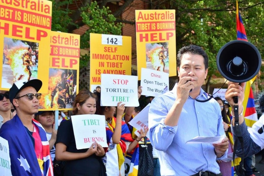 A man with a megaphone in a protest with signs asking Australia to help Tibet.