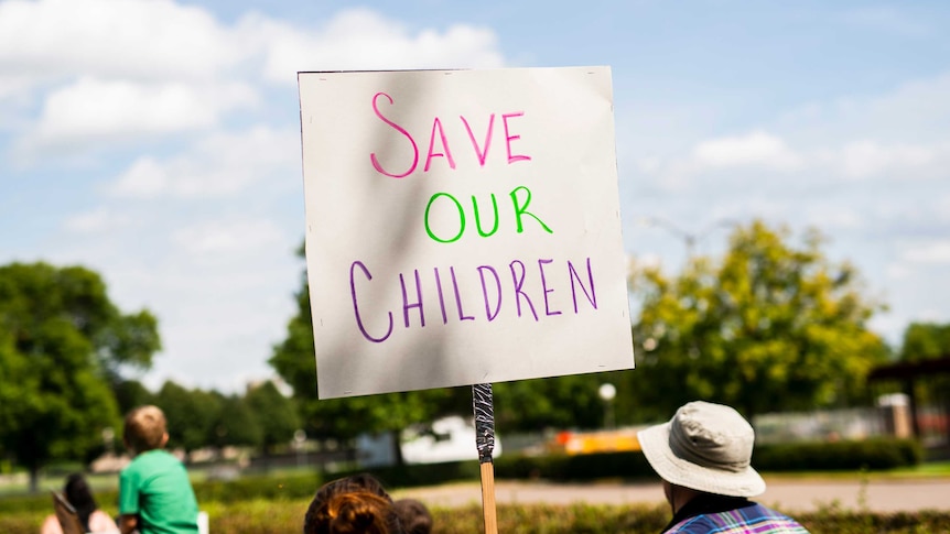 A sign at a protest that says "Save Our Children".