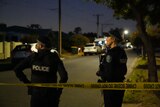 Two police officers stand in front of crime scene tape in a dark street