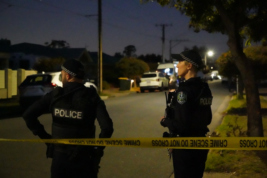 Two police officers stand in front of crime scene tape in a dark street