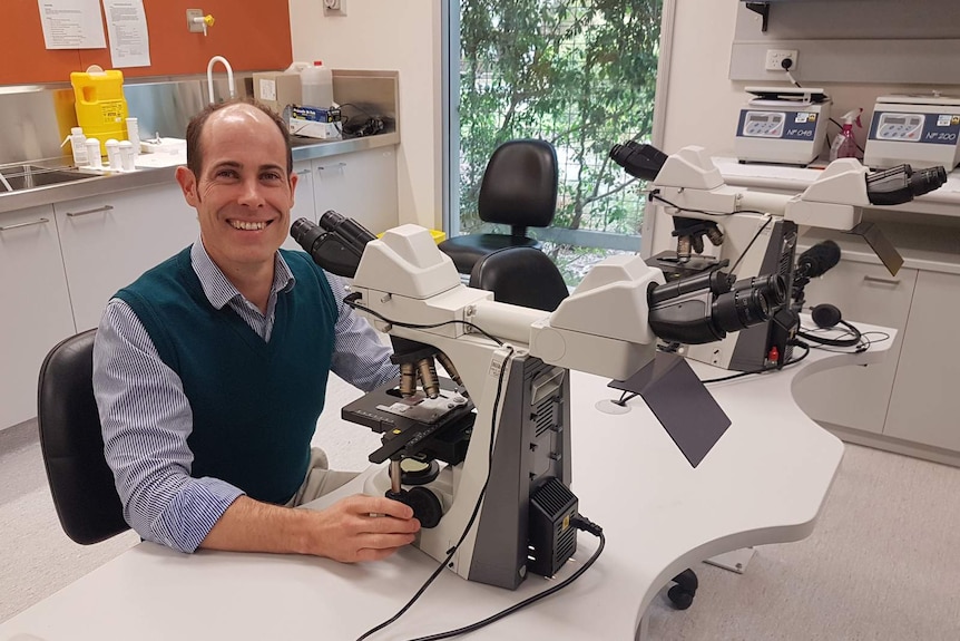 A photo of a man sitting in front of a microscope.