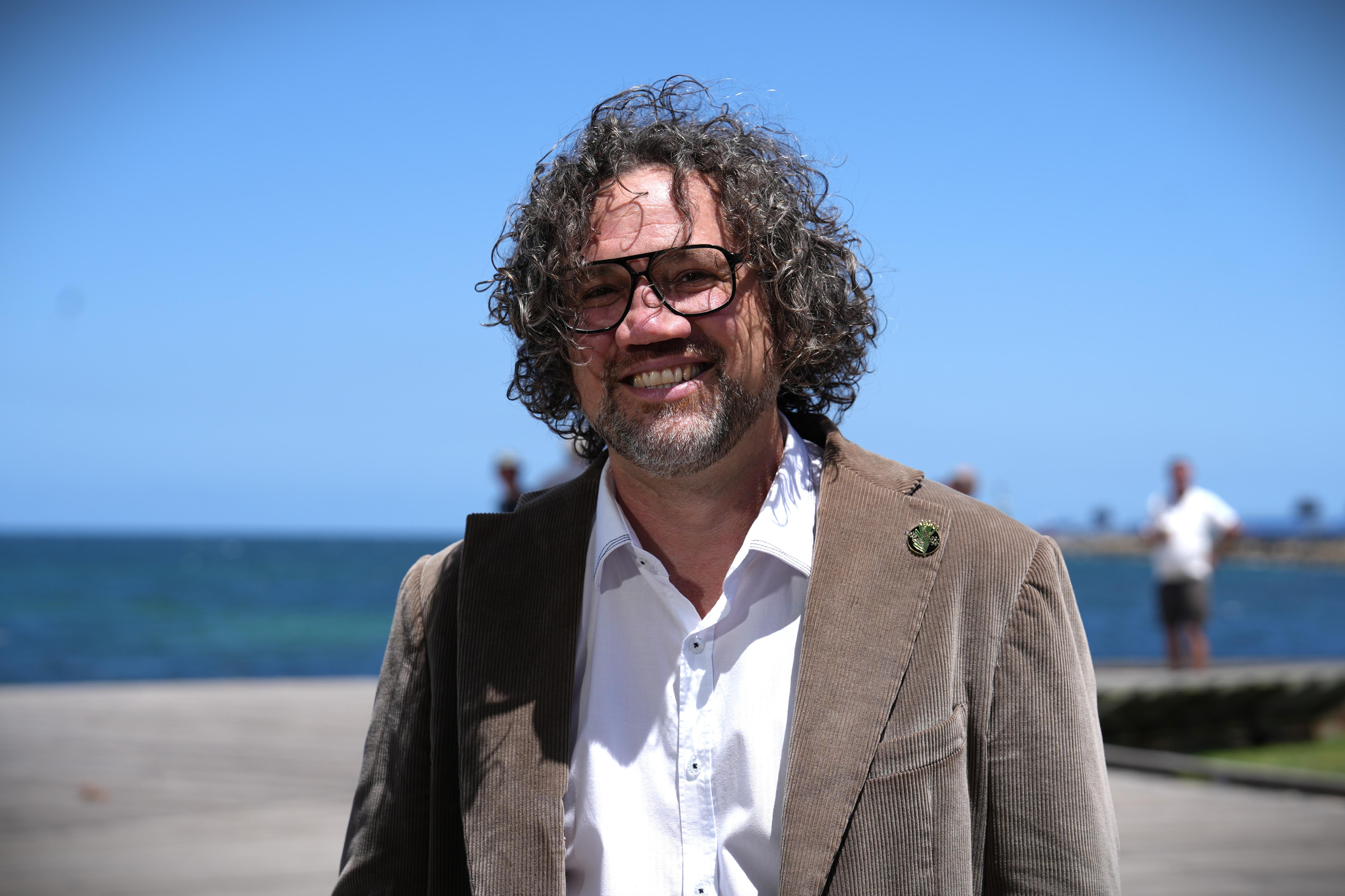 El alcalde de la ciudad de Fremantle, Ben Lawver, sonríe con el agua y el cielo azul de fondo.