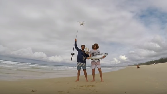 on the beach, one man with holding a drone and one man holding a tuna