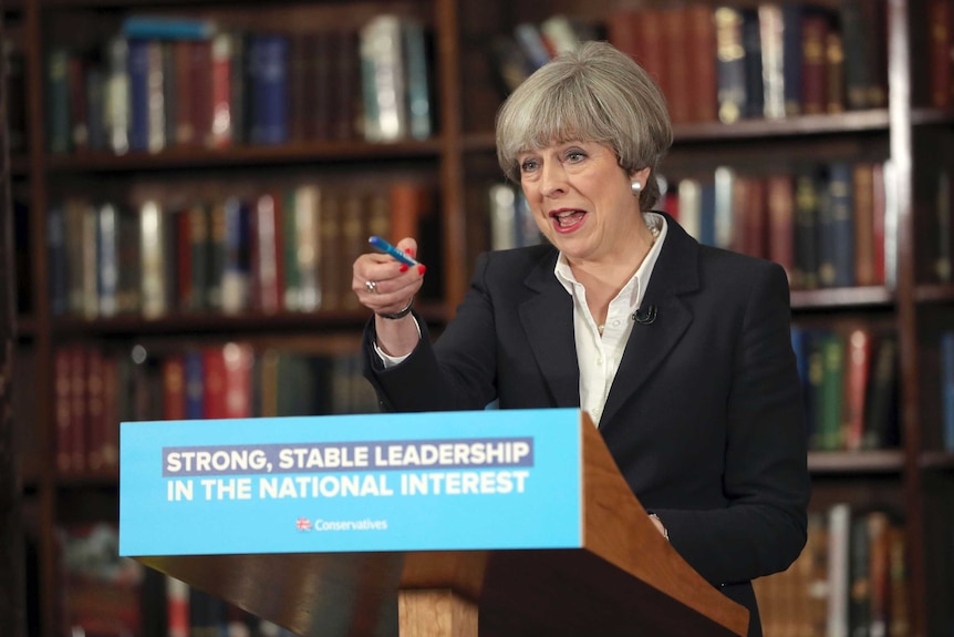 Theresa May points while standing at a lectern to deliver a speech.