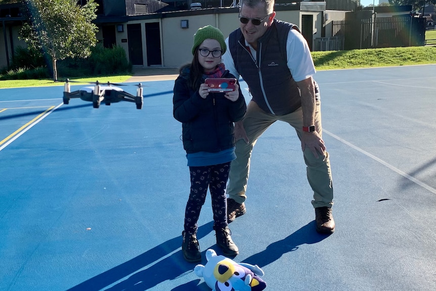 A child and a man play with a drone.