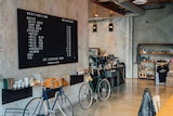Bikes lean up against an internal concrete wall, under a large black cafe menu.