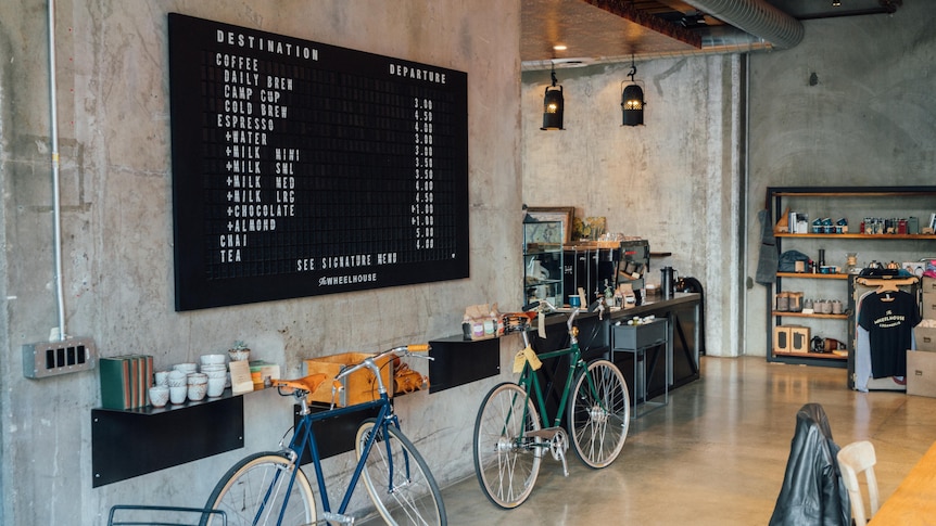 Bikes lean up against an internal concrete wall, under a large black cafe menu.