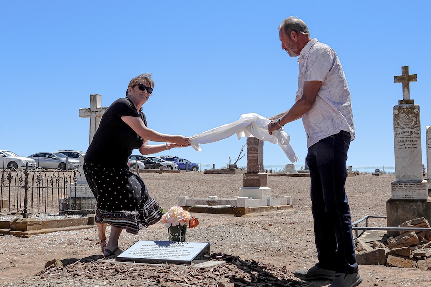 Two people hold either end of a piece of white material. A grave headshot has been unveiled.