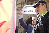Robbie Katter holds a "condemn Hamas" sign at pro-Palestine protest in front of Queensland Parliament.