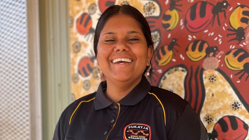 A young Aboriginal woman smiling as she holds a brightly coloured picture book.