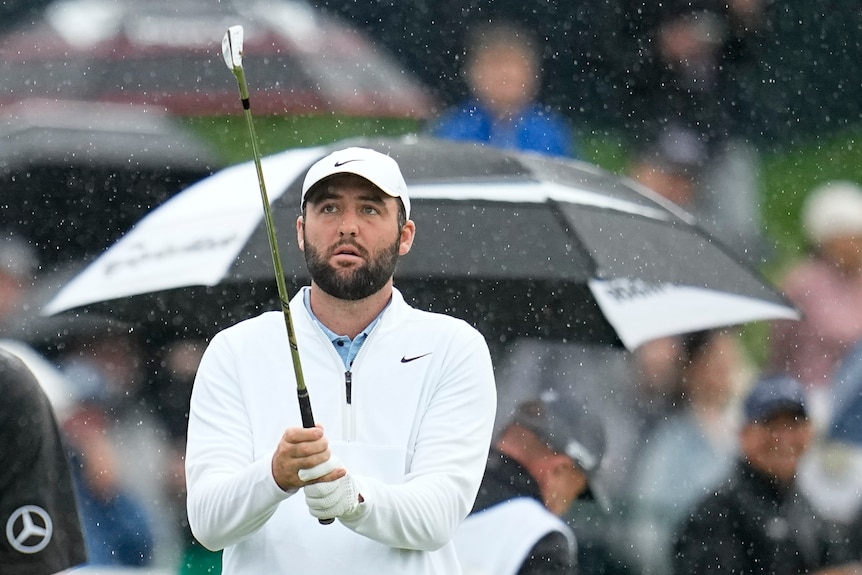 Scottie Scheffler holds his golf club while standing in the rain on the practise range.