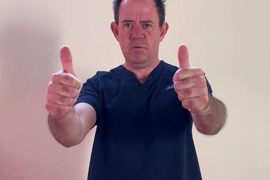 Jonathan Papson wearing navy blue scrubs gives two thumbs up in a dance video.