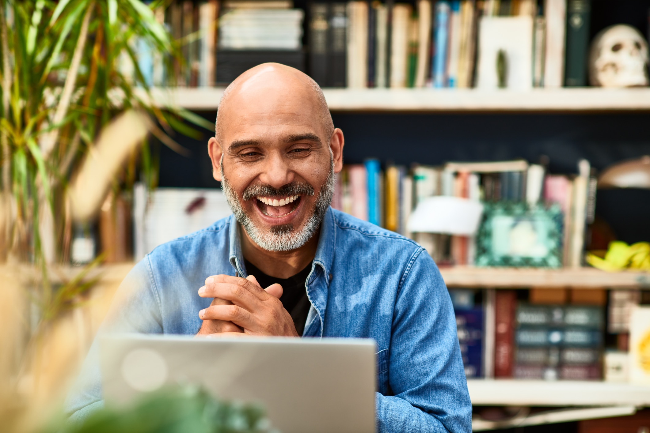 Man laughing and smiling and clasping his hands in front of laptop screen