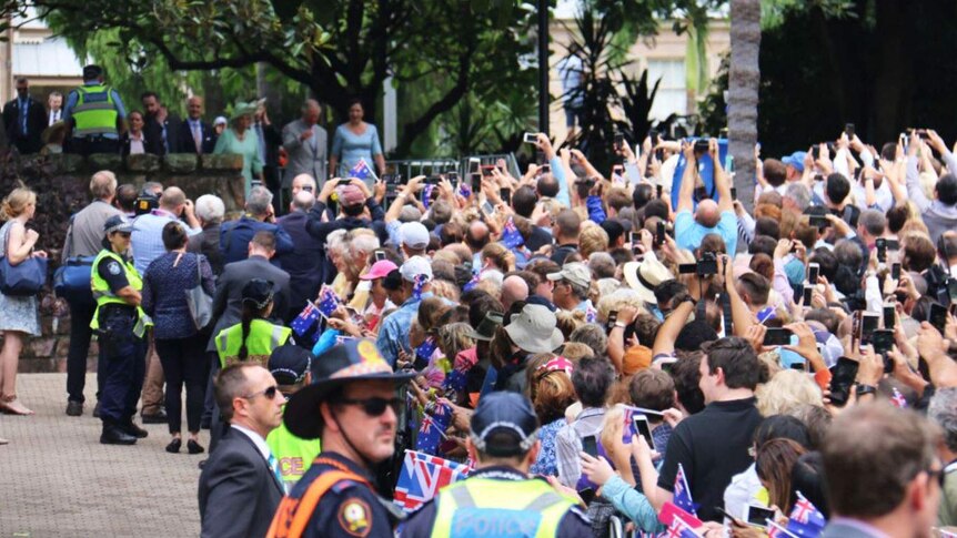 A crowd of people pointing phones and cameras toward Prince Charles and the Duchess of Cornwall