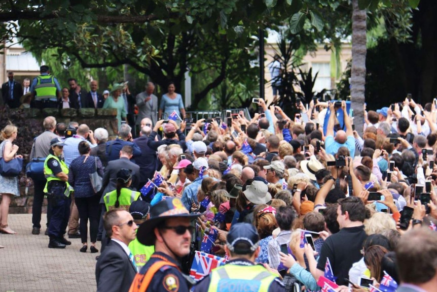 A crowd of people pointing phones and cameras toward Prince Charles and the Duchess of Cornwall