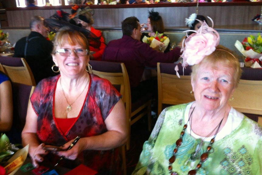 Two women sitting down smiling at a special event, wearing fascinators.