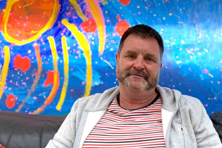 A man looking at the camera with bright artwork behind him