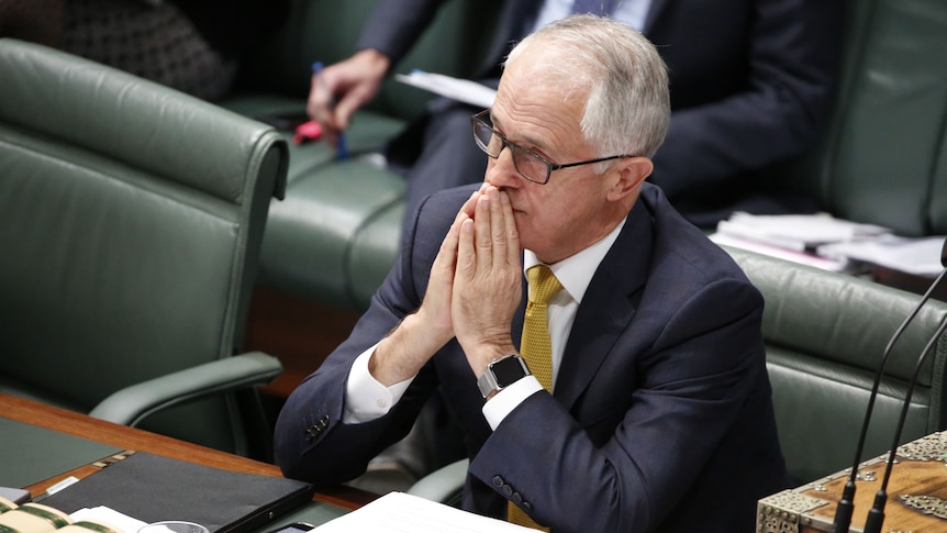 Prime Minister Malcolm Turnbull sits in Parliament with his hands to his mouth.