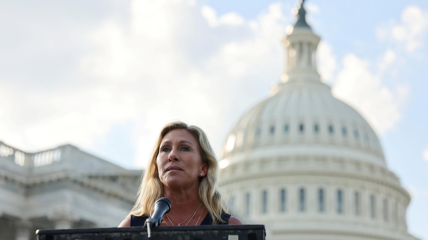 Representative Marjorie Taylor Greene stands at a lectern in front of Capitol building in the United States  