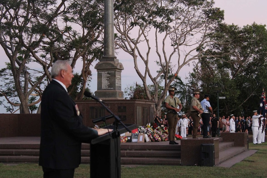 A man speaks into a microphone as soldiers stand at the cenotaph.