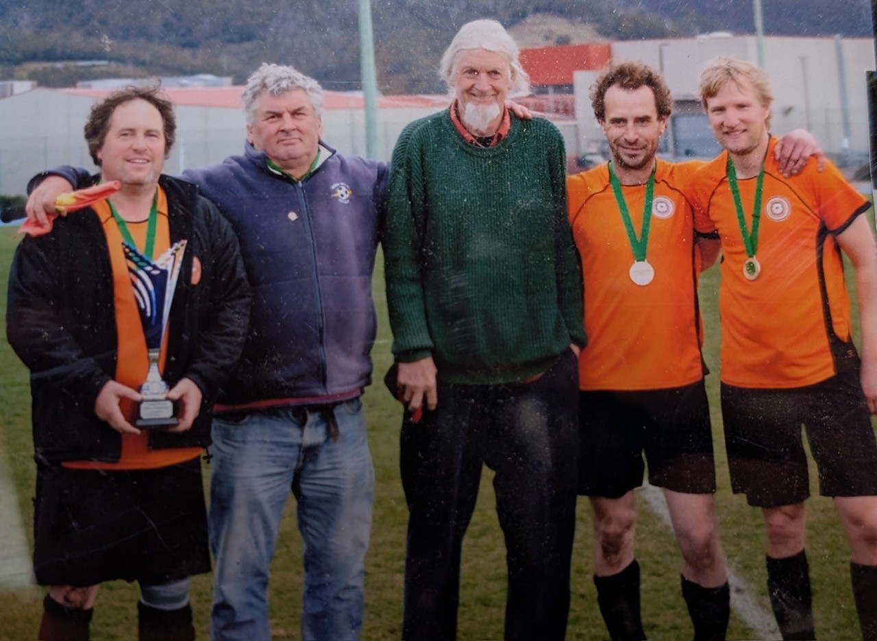 Five men of varying ages stand with arms around each other
