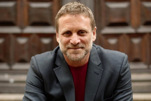 Man wearing a red shirt and grey-blue blazer. 