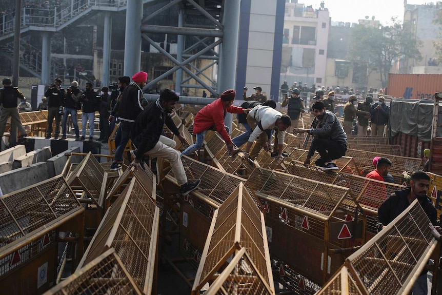 People climb over large yellow barricades in the streets of New Delhi