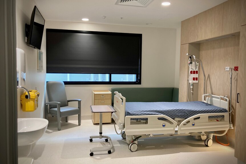 An empty hospital room with a bed, lounge, TV, basin and couch. 