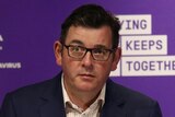 Daniel Andrews, dressed in a shirt and jacket, delivers a press conference in front of a purple background.